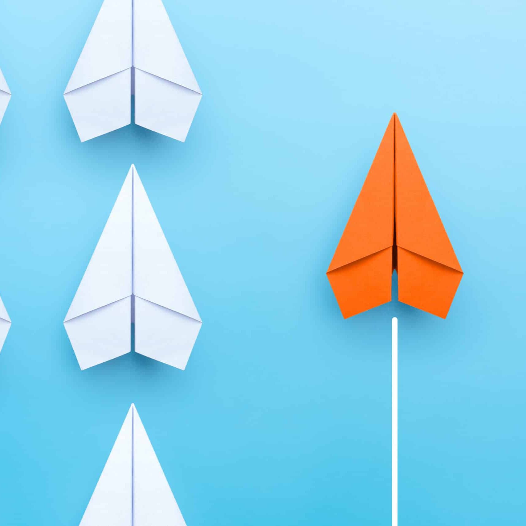 business concept for new ideas creativity and innovative solution, group of white paper plane in one direction and one orange paper plane pointing in different way on blue background